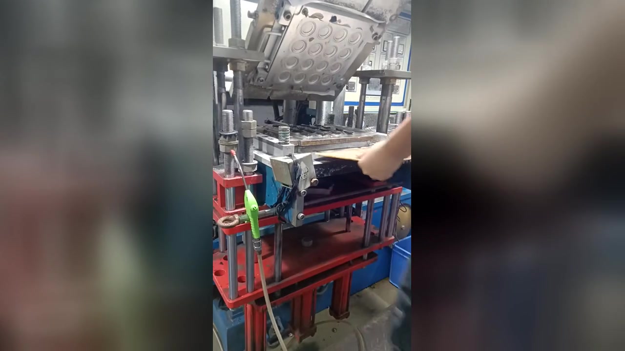An open mould with round cavities inside a blue compression moulding press.