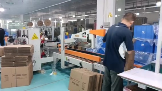 An operator positioning a carton beside an orange carton-sealing machine.