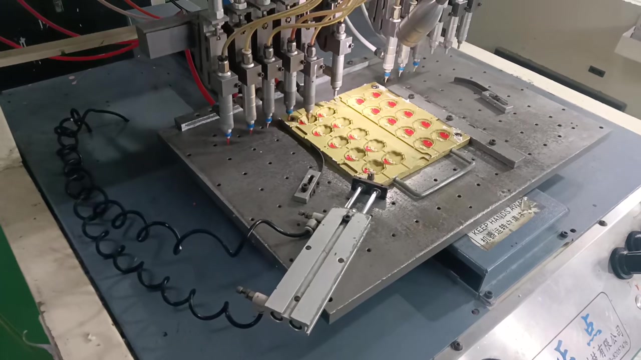 Multiple dispensing nozzles positioned over a mould with coloured silicone details.