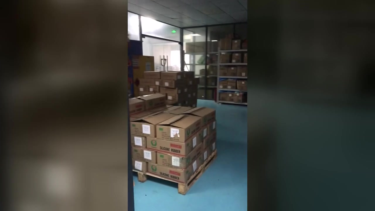 Cartons labelled silicone rubber stacked on pallets beside shelving in a storage area.