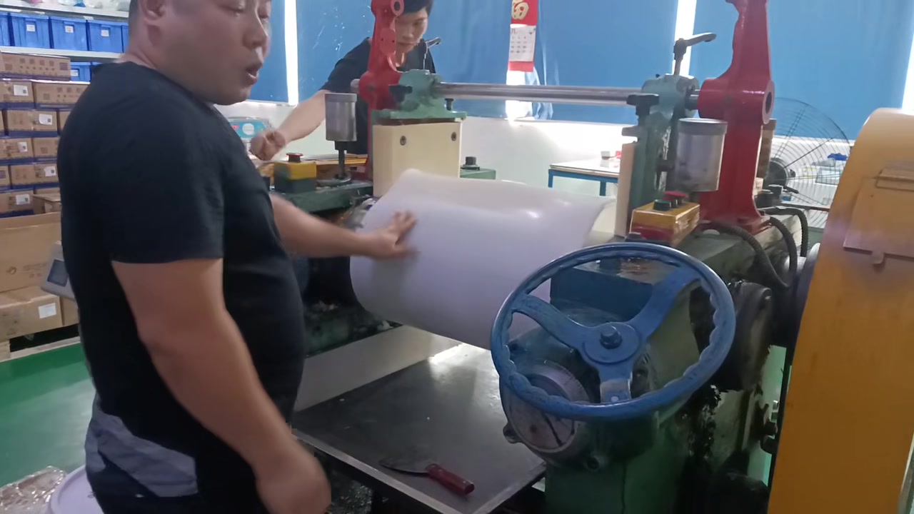 An operator handling a pale silicone sheet on the rollers of a mixing mill.