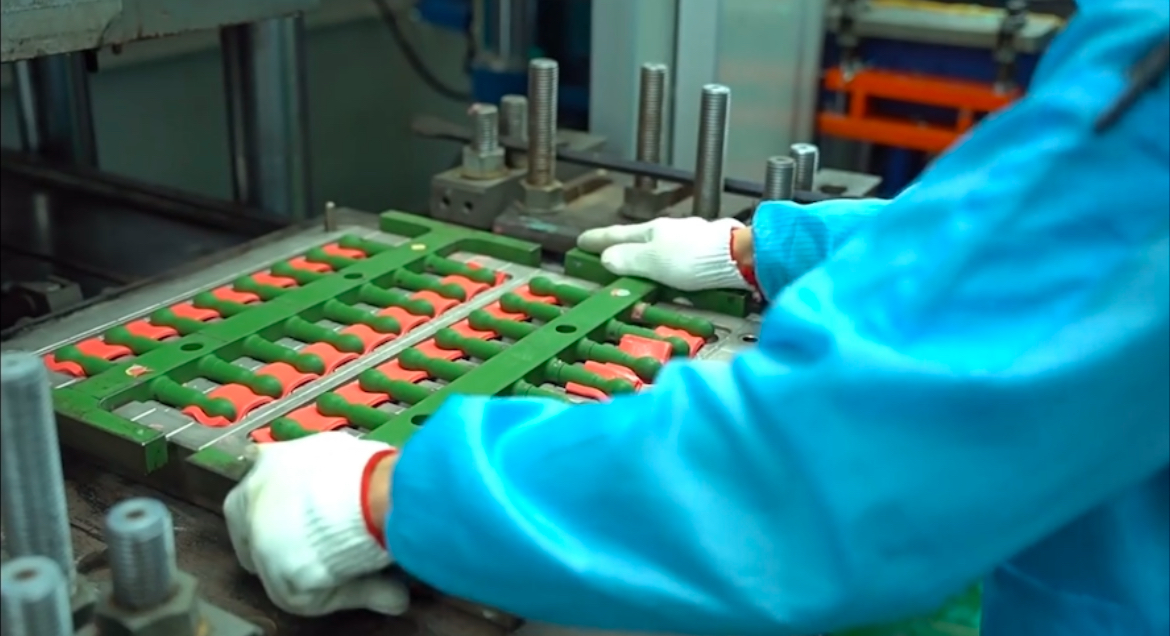 Operator handling a multi-cavity mold with colored silicone products at a molding press