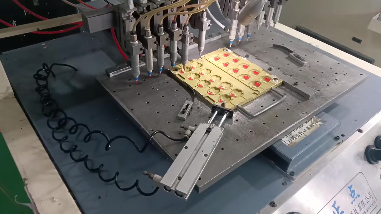 Multiple dispensing heads above a mould with yellow, red and green silicone details on a production machine.